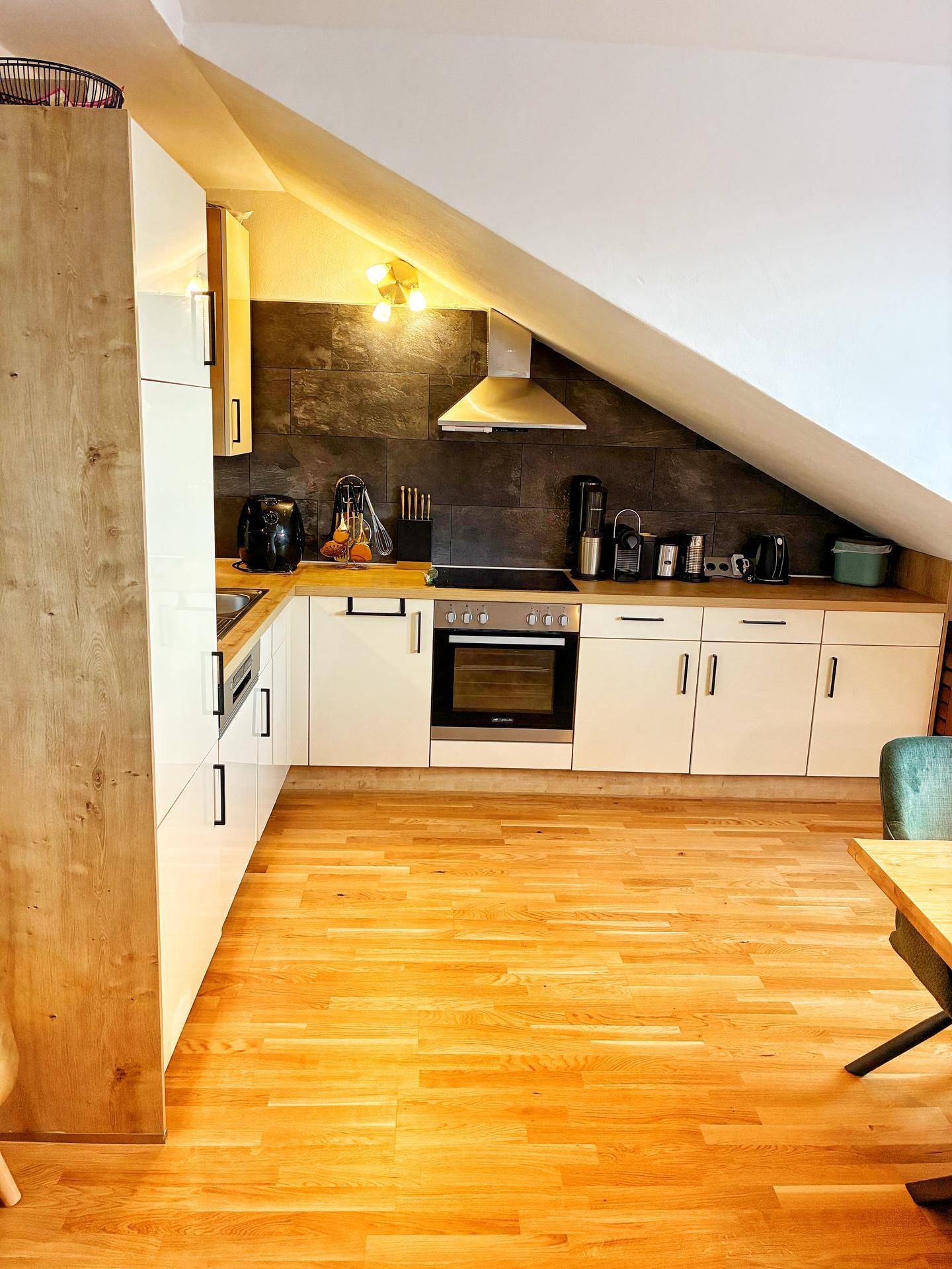 Moderne Einbauküche mit hellen Fronten, Holz-Arbeitsplatte und integrierten Geräten unter der Dachschräge.