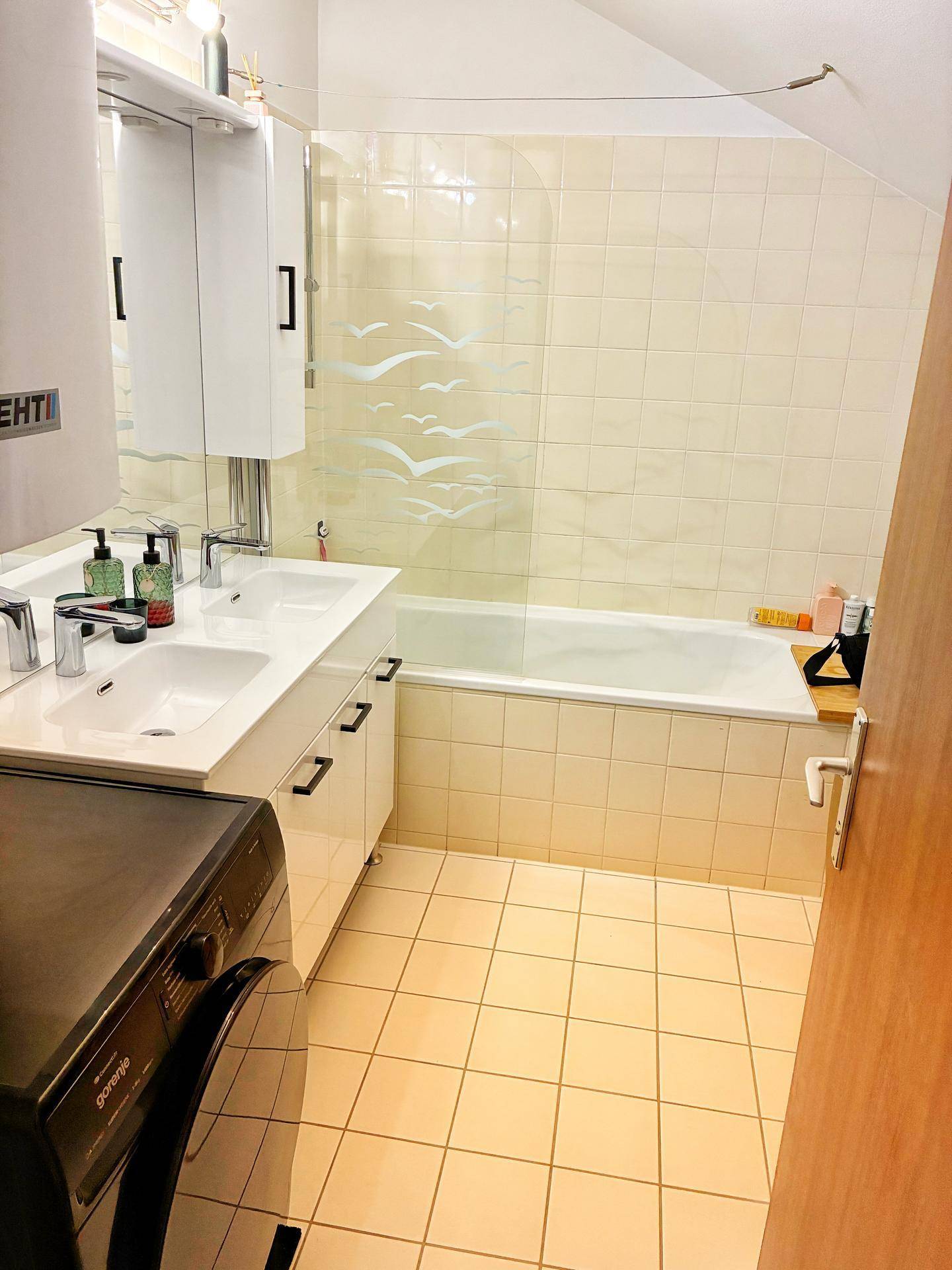 Helles Badezimmer mit Doppelwaschbecken, Badewanne und Waschmaschine unter der Dachschräge.