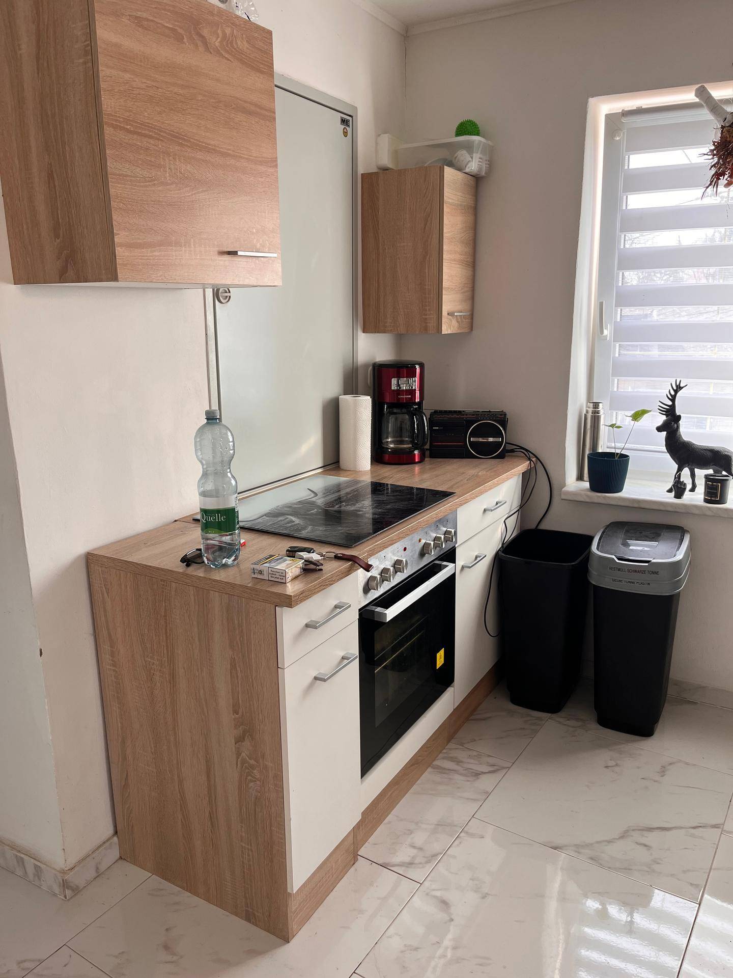 Kleine Küche mit Holz- und weißen Fronten, Induktionskochfeld und Fenster mit Jalousien.
