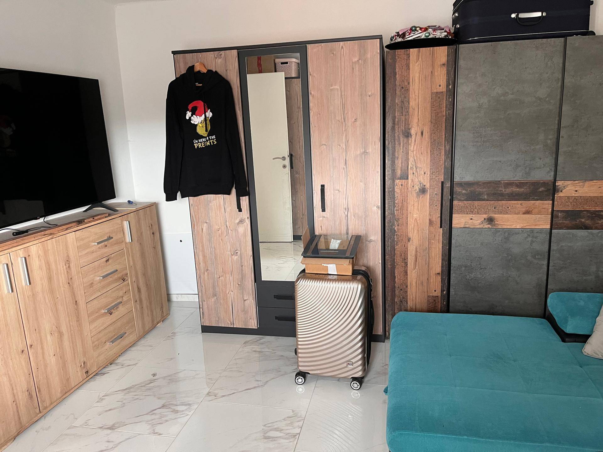 Wohnbereich mit großem Kleiderschrank, Sofa und Fernseher auf hellen Fliesen.