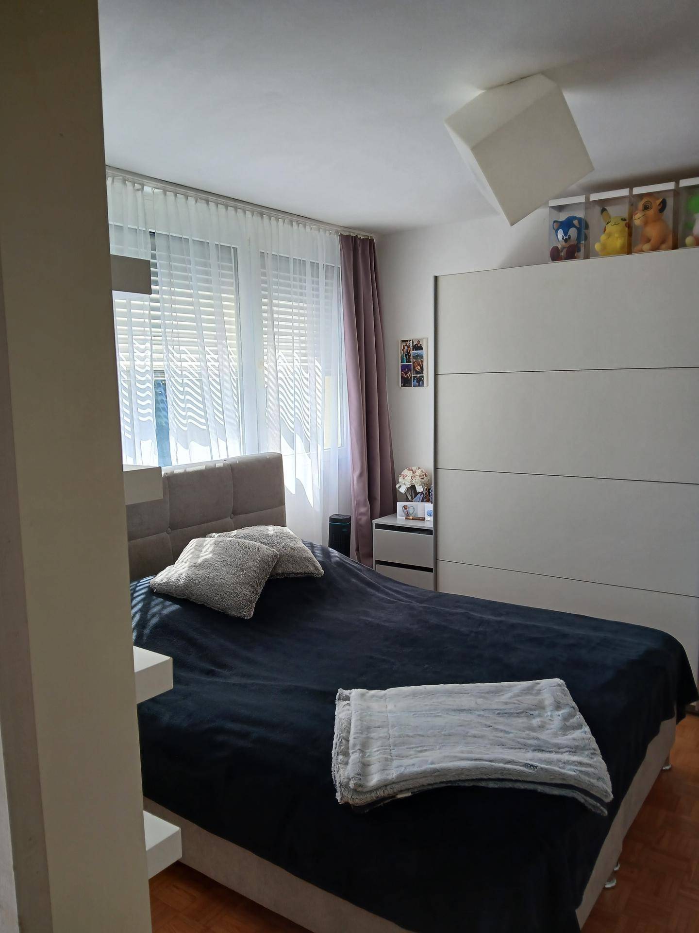 Gemütliches Schlafzimmer mit großem Bett, weißem Kleiderschrank und hellen Vorhängen am Fenster.