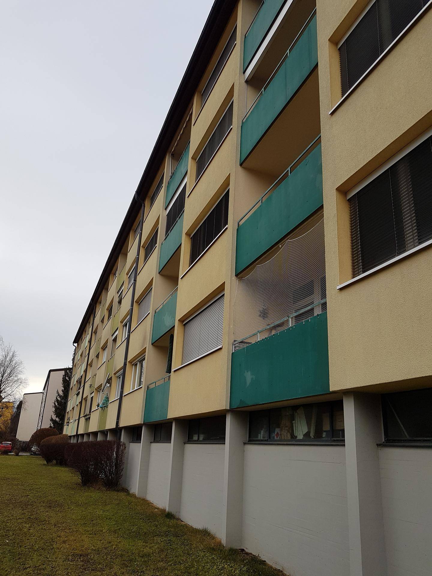 Langes Mehrfamilienhaus mit gelber Fassade, grünen Balkonen und einer Rasenfläche davor.