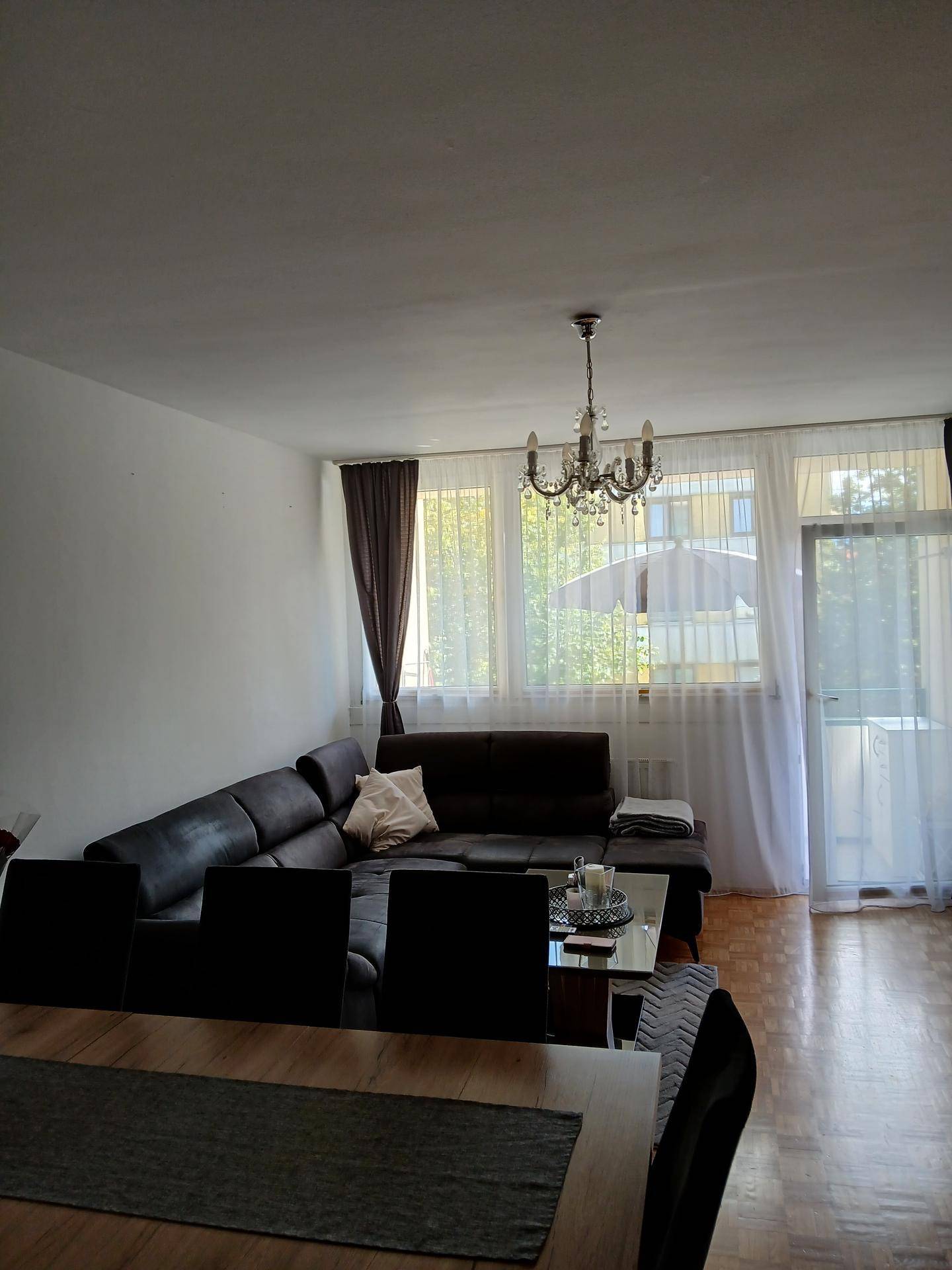 Geräumiges Wohnzimmer mit dunklem Ecksofa, Kronleuchter und großen Fenstern.