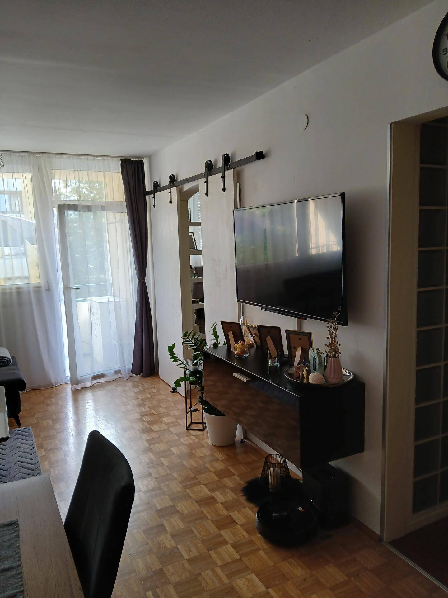 Wohnbereich mit Fernseher, Schiebetür und Zugang zu einem Balkon oder einer Terrasse.