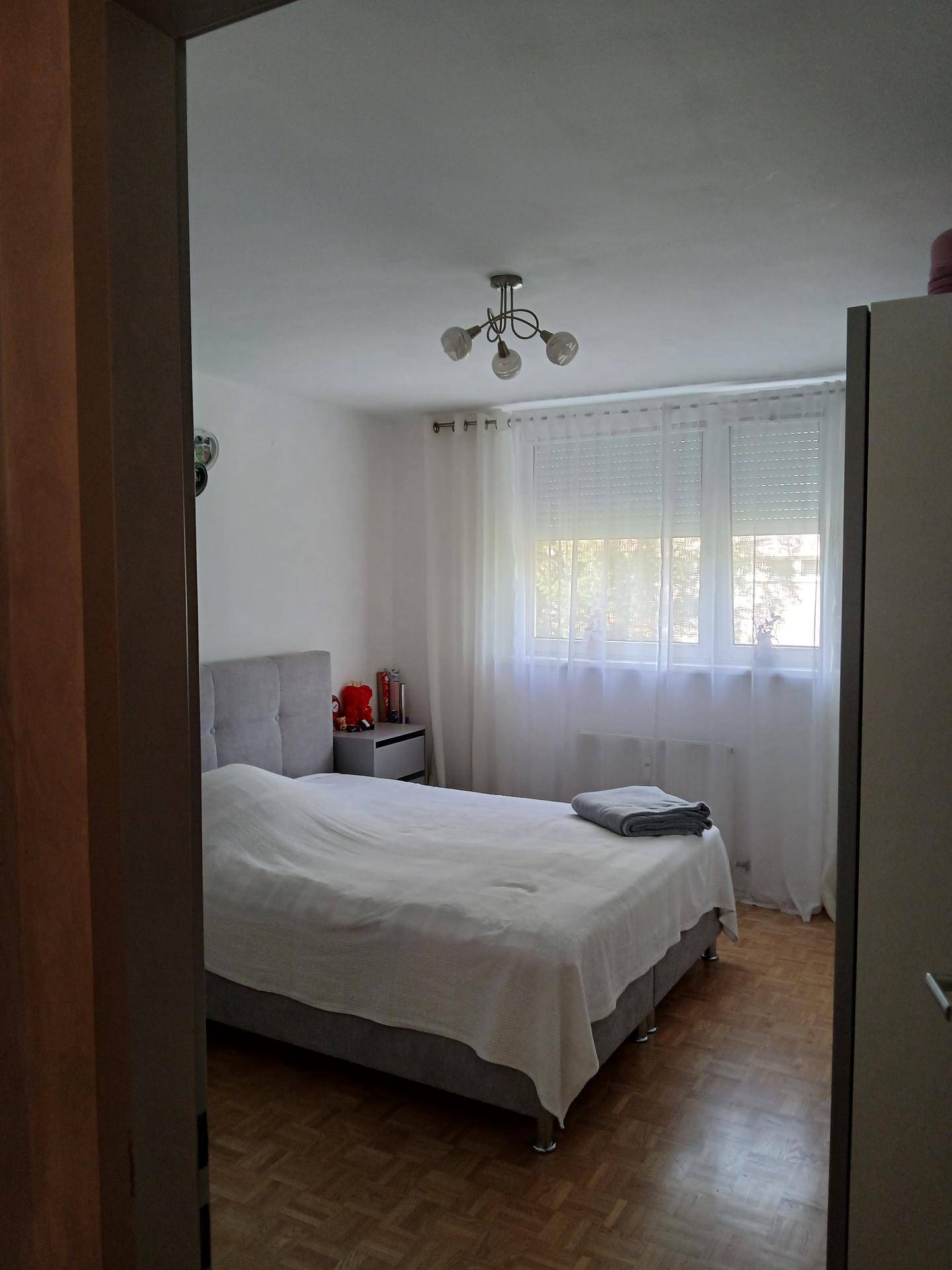 Helles Schlafzimmer mit Doppelbett, Nachttisch und Parkettboden, durch eine Türöffnung gesehen.