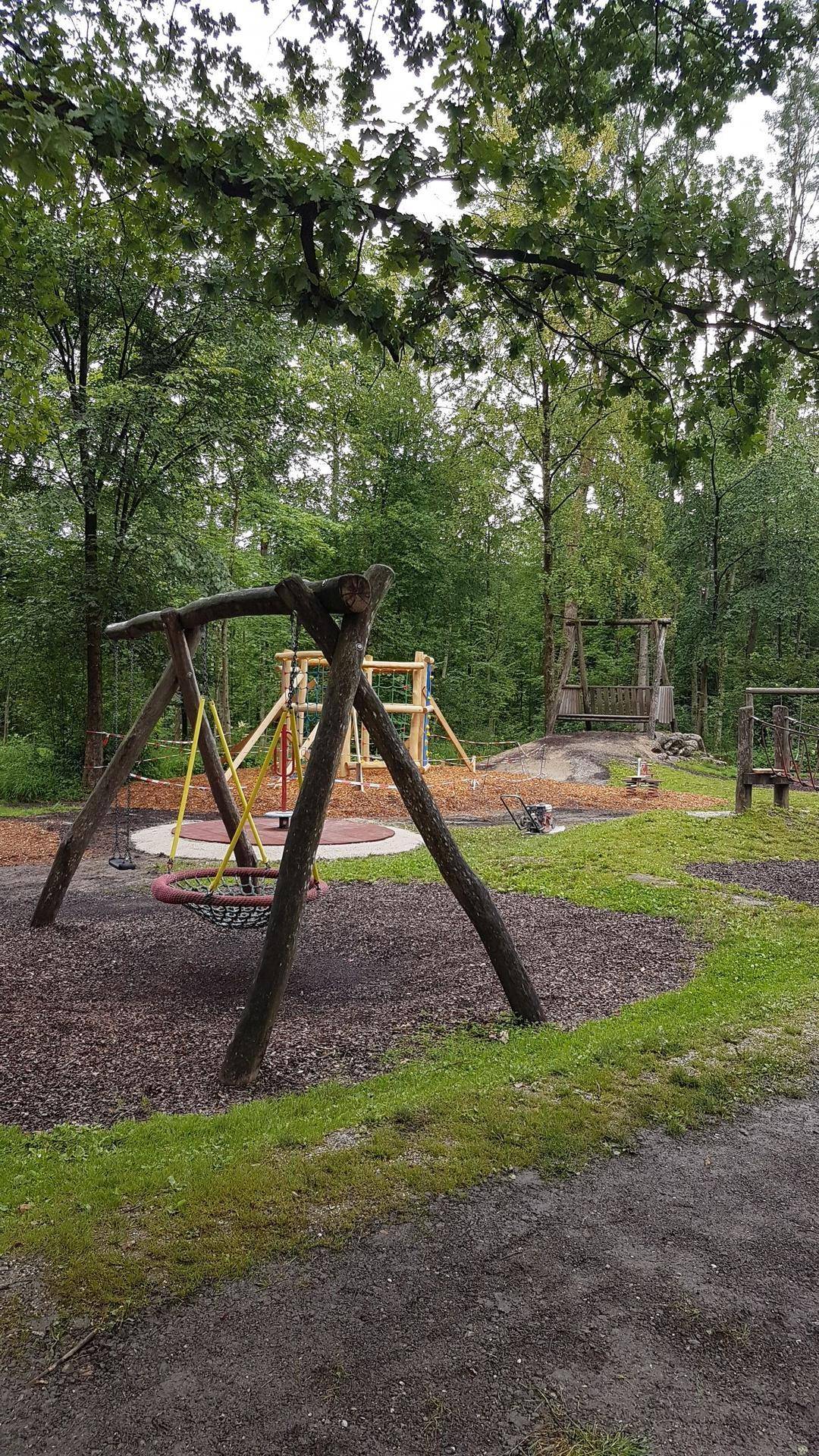 Naturnaher Spielplatz im Wald mit verschiedenen Holzschaukeln und Spielgeräten für Kinder.