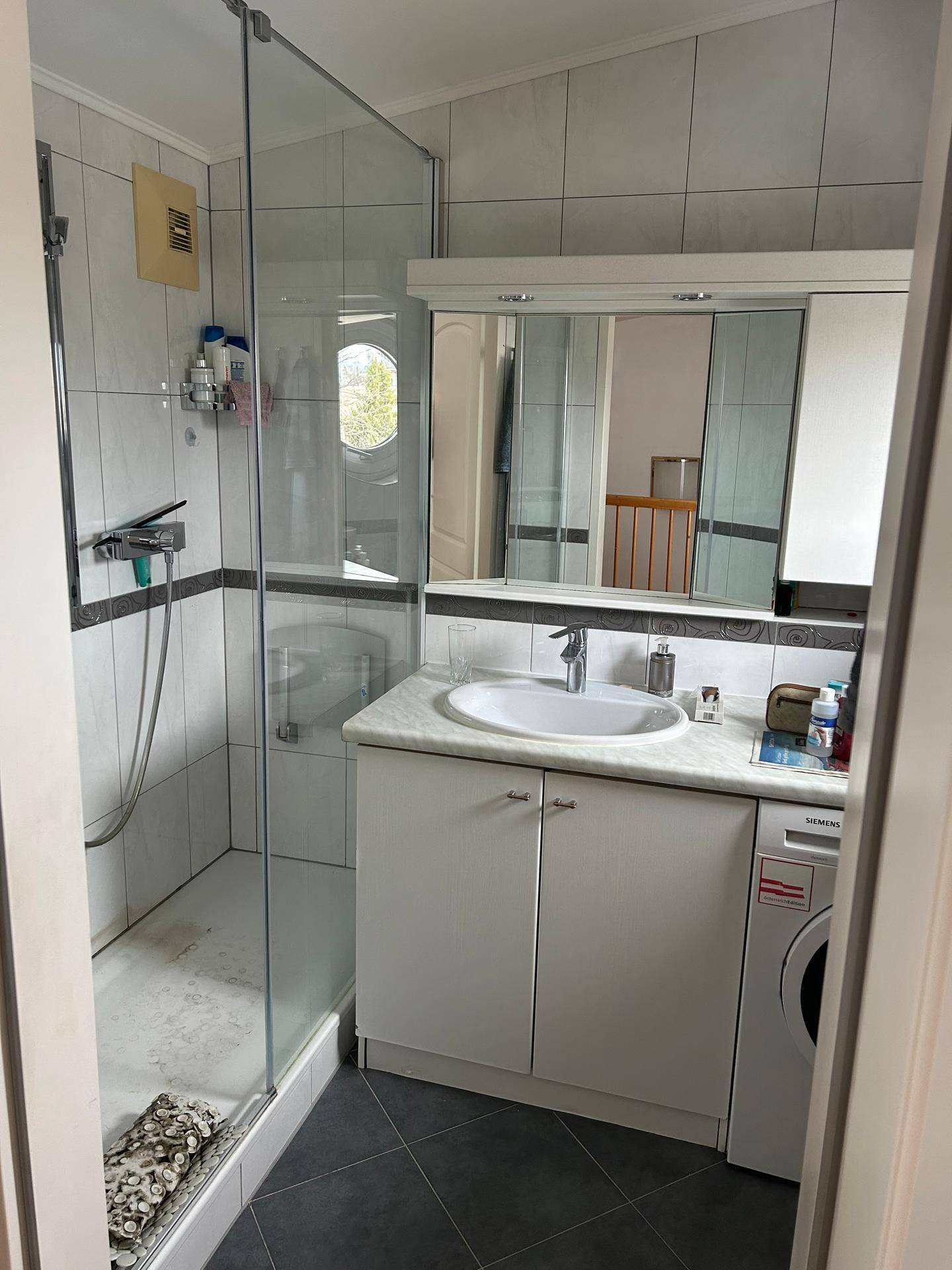 Badezimmer mit Duschkabine, Waschbecken, Spiegelschrank und integrierter Waschmaschine.