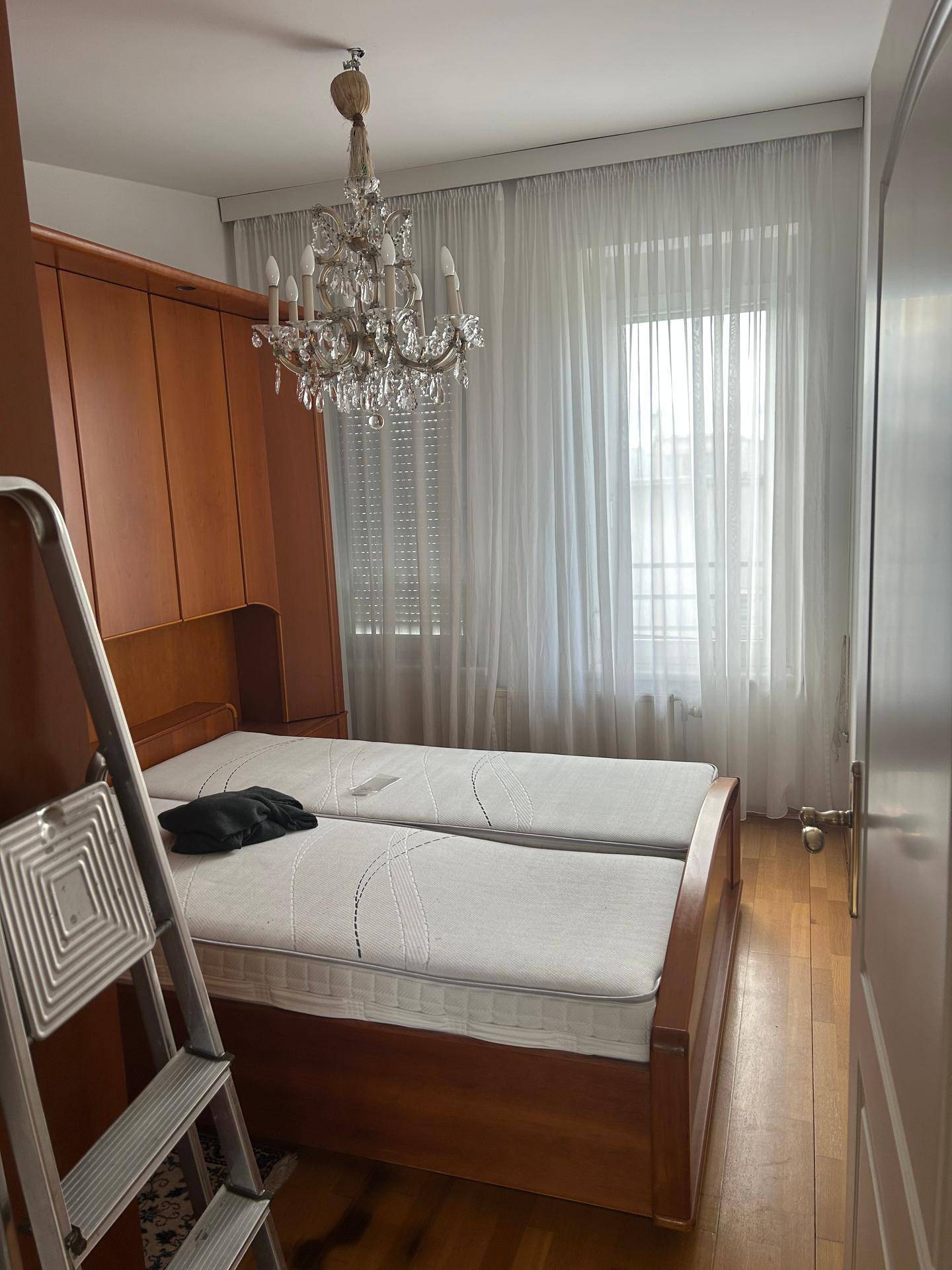 Schlafzimmer mit zwei Einzelbetten, Holzmöbeln und einem eleganten Kronleuchter.
