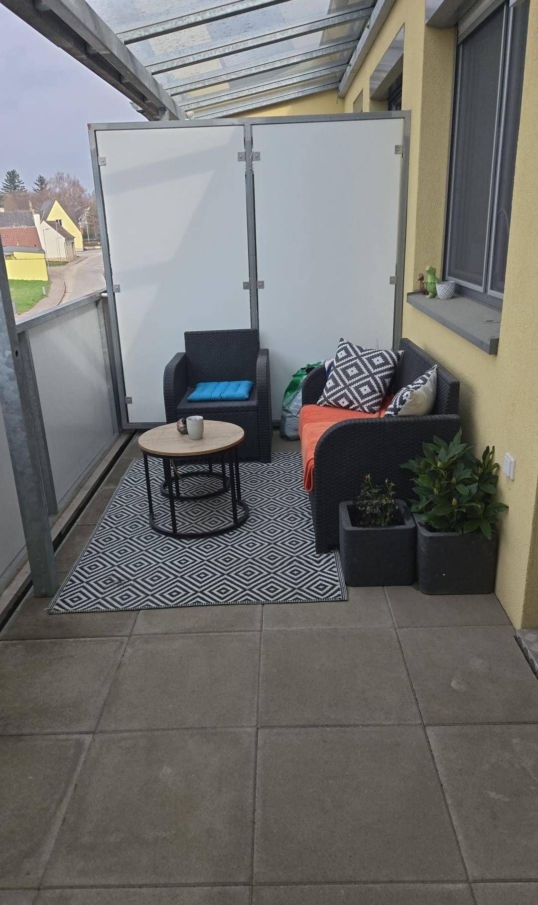 Gemütlicher Balkon mit Fliesenboden, Sitzgelegenheiten und einem kleinen Tisch, teilweise überdacht.
