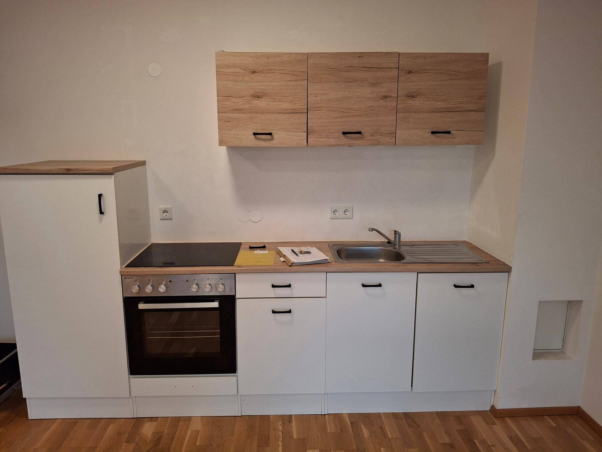 Kleine Einbauküche mit weißen Unterschränken, Holz-Arbeitsplatte und integrierten Geräten.