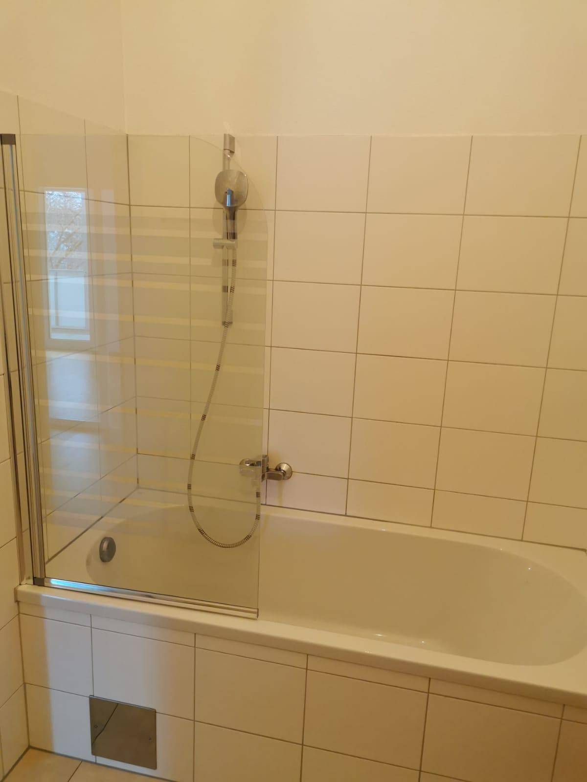 Badezimmer mit Badewanne, Duschabtrennung aus Glas und weißen Fliesen an den Wänden.