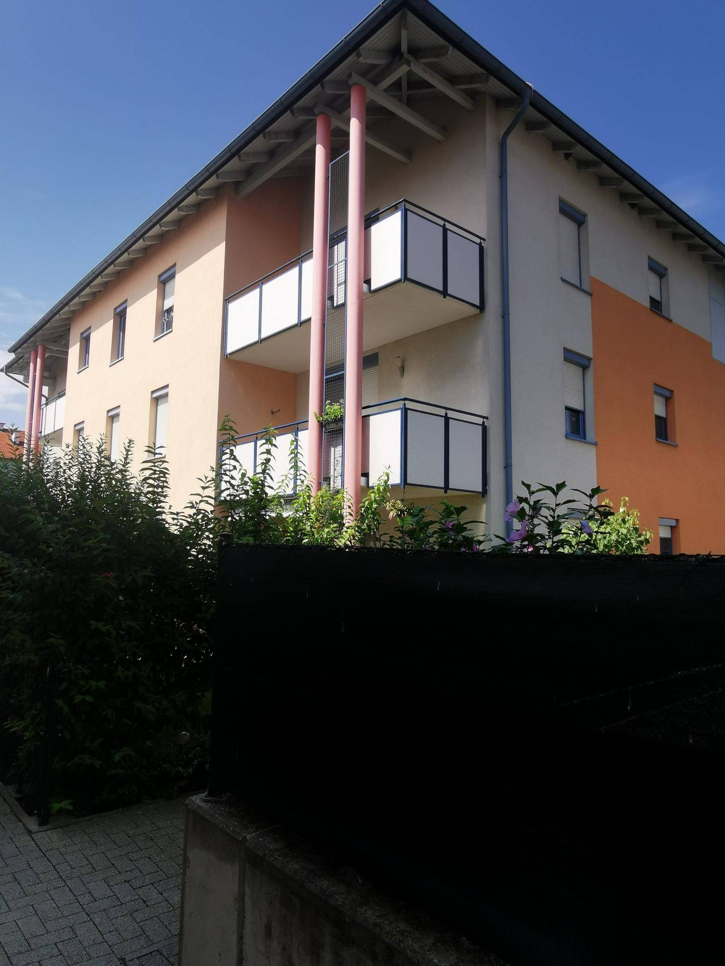 Nahaufnahme der Gebäudefassade mit mehreren Balkonen und farbigen Säulen unter blauem Himmel.
