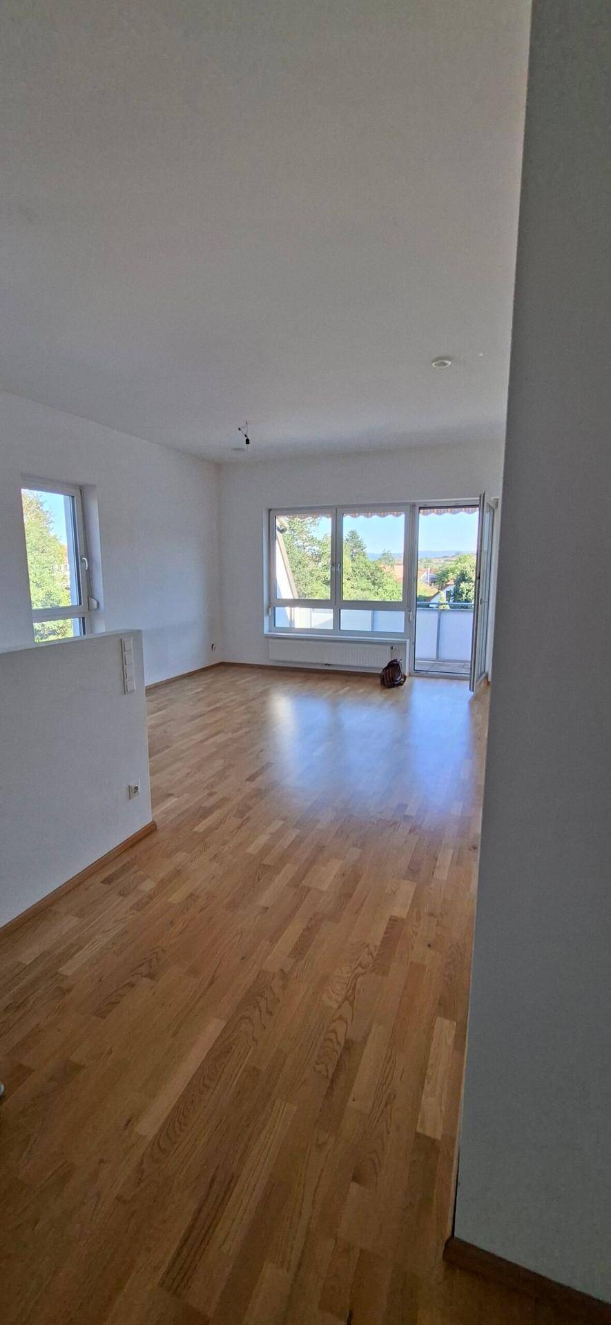 Geräumiges Wohnzimmer mit Holzboden, großen Fenstern und Zugang zu einem Außenbereich.