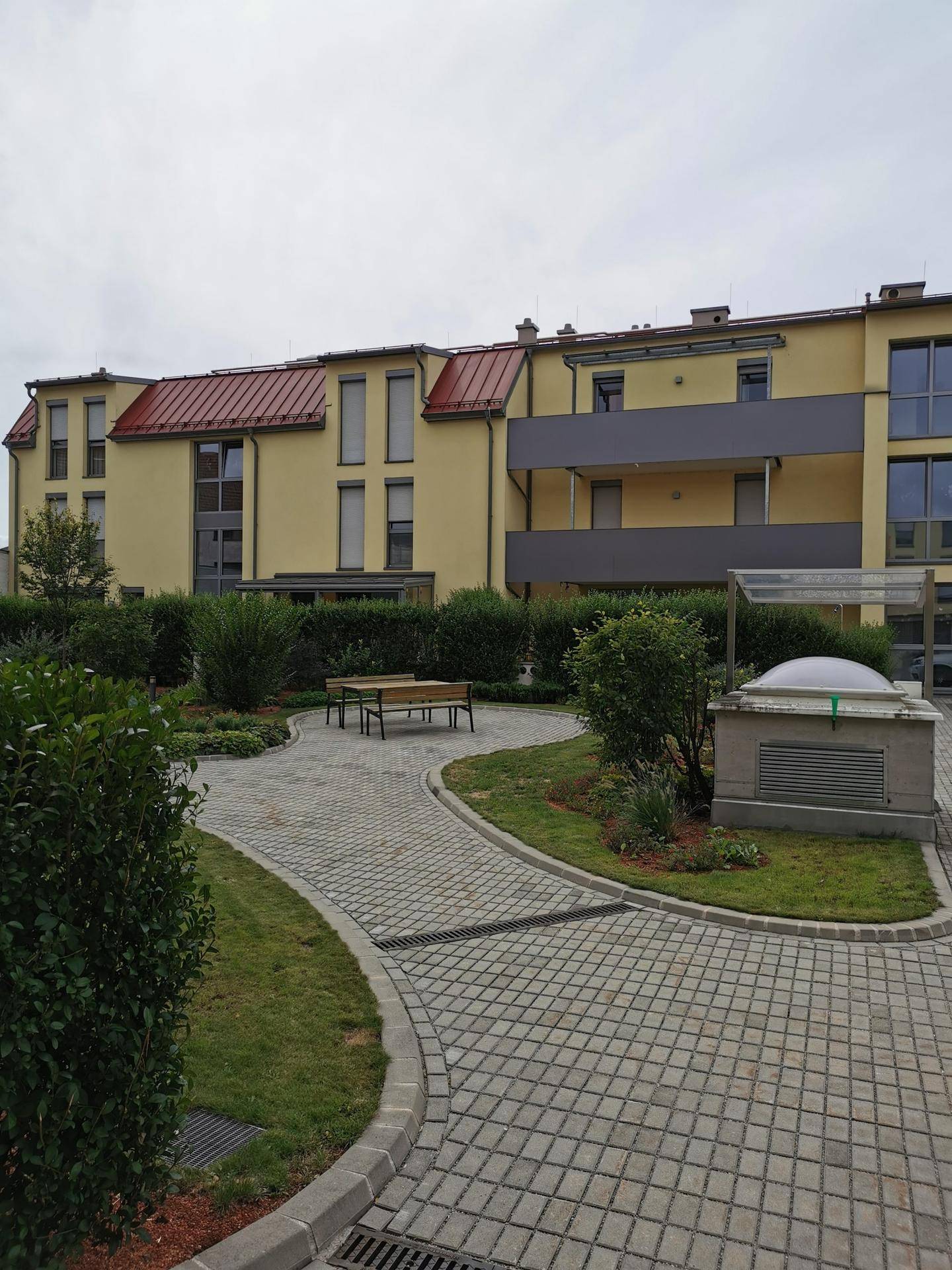 Gepflegter Gemeinschaftsgarten mit Bänken und gepflasterten Wegen zwischen den Wohngebäuden.
