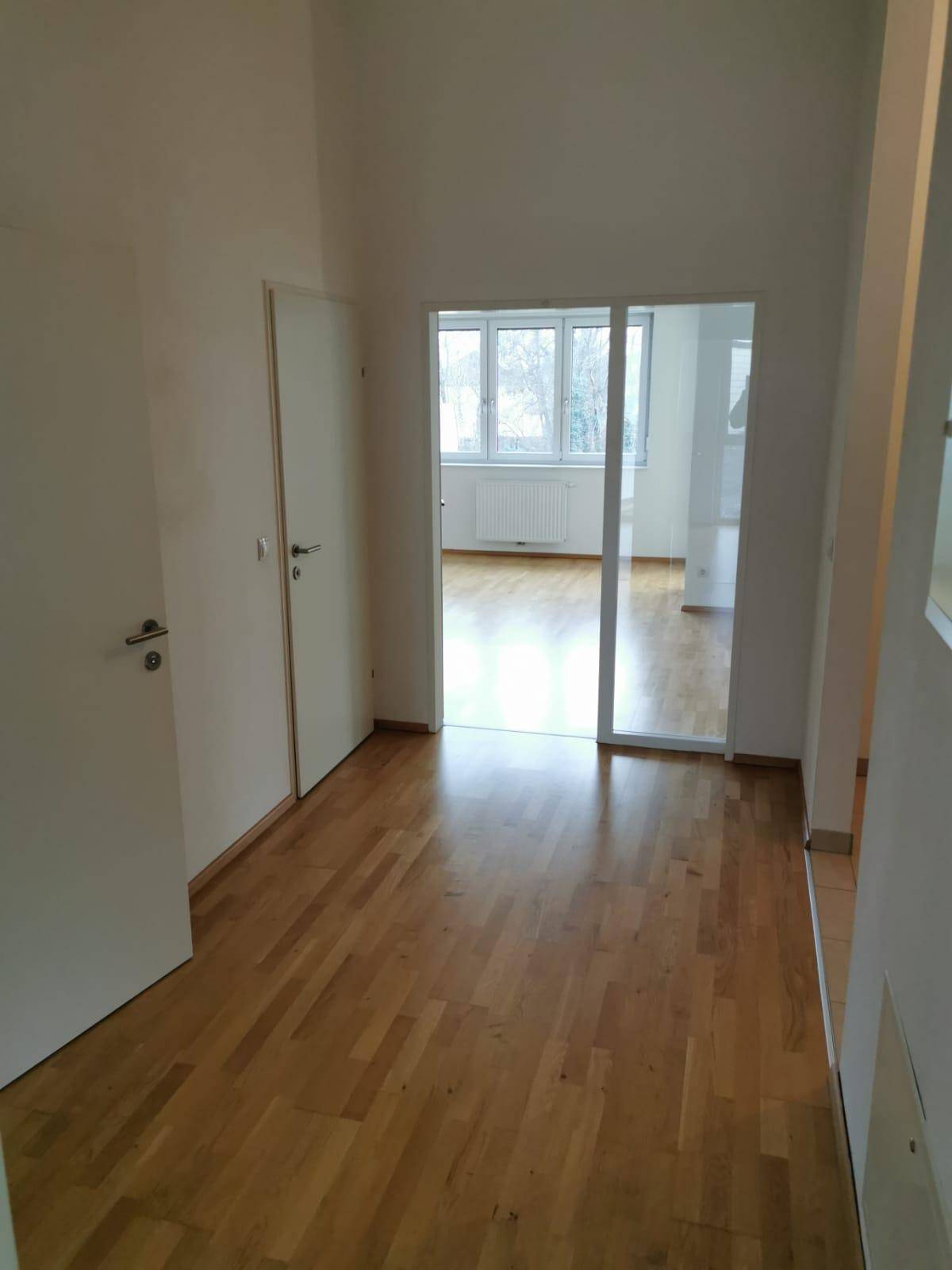 Heller Flur mit Holzparkettboden und weiß gestrichenen Wänden, der zu einem weiteren Raum führt.