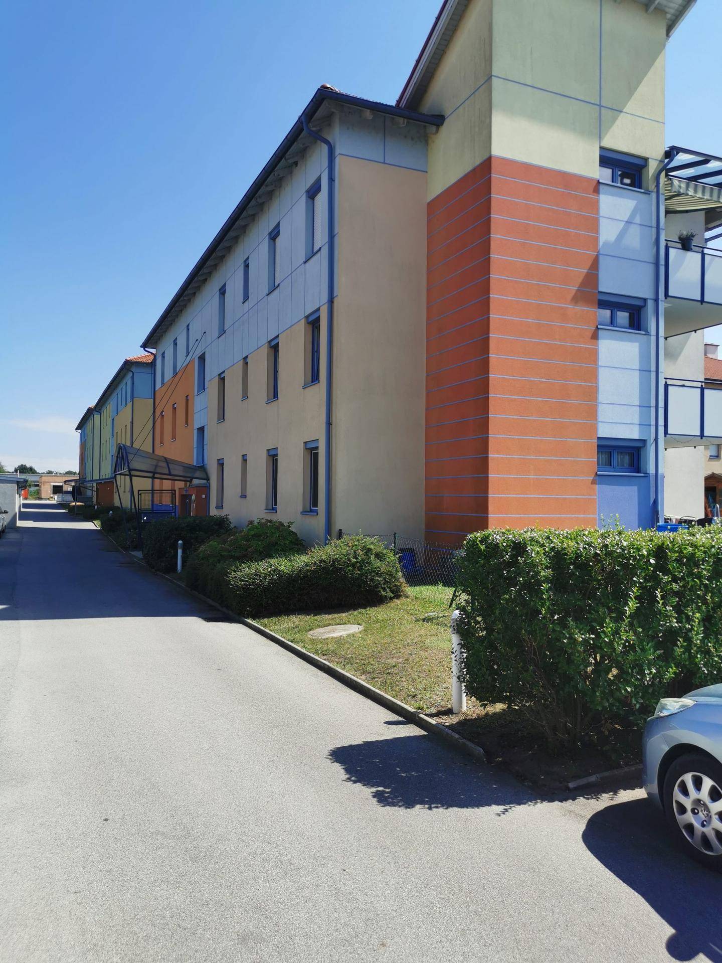 Seitenansicht eines mehrstöckigen Wohngebäudes mit farbigen Fassadenelementen und einer Zufahrtsstraße.