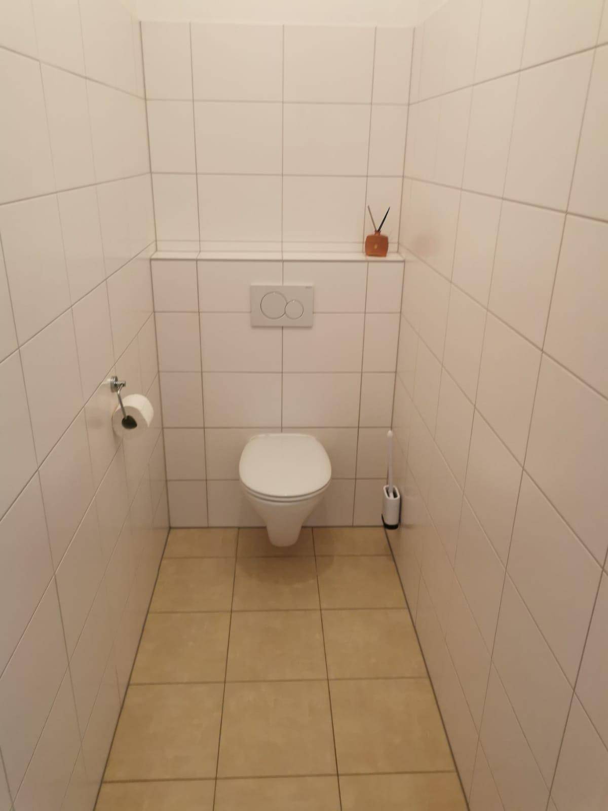 Separates WC mit wandhängender Toilette und weißen Fliesen an Wänden und Boden.