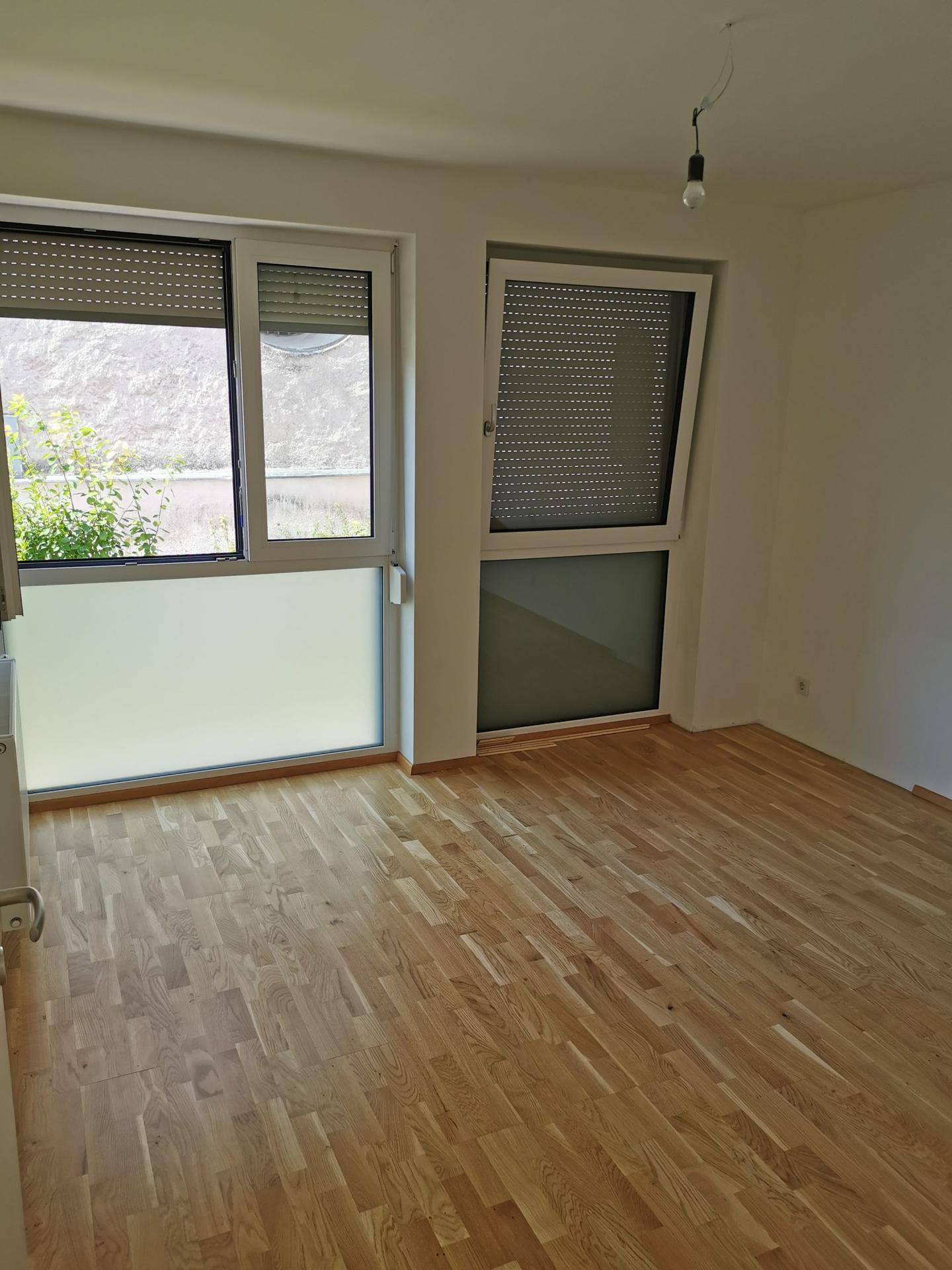 Heller Raum mit Holzboden und Fenstern, ausgestattet mit praktischen Rollläden für Privatsphäre.