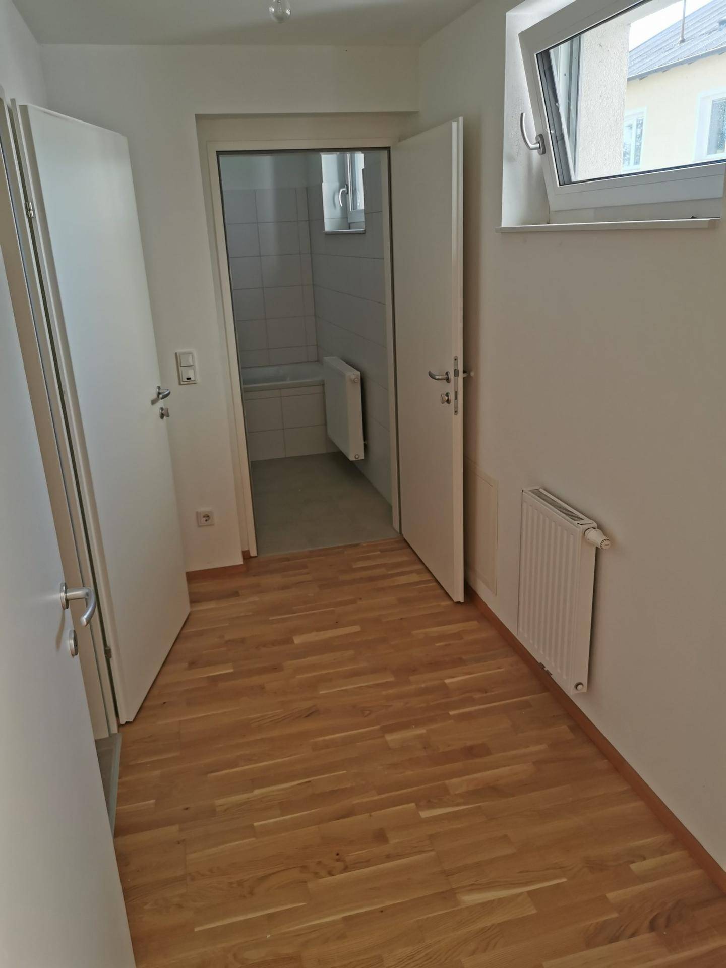 Heller Flur mit Holzboden und Fenster, der zu einem Badezimmer führt.