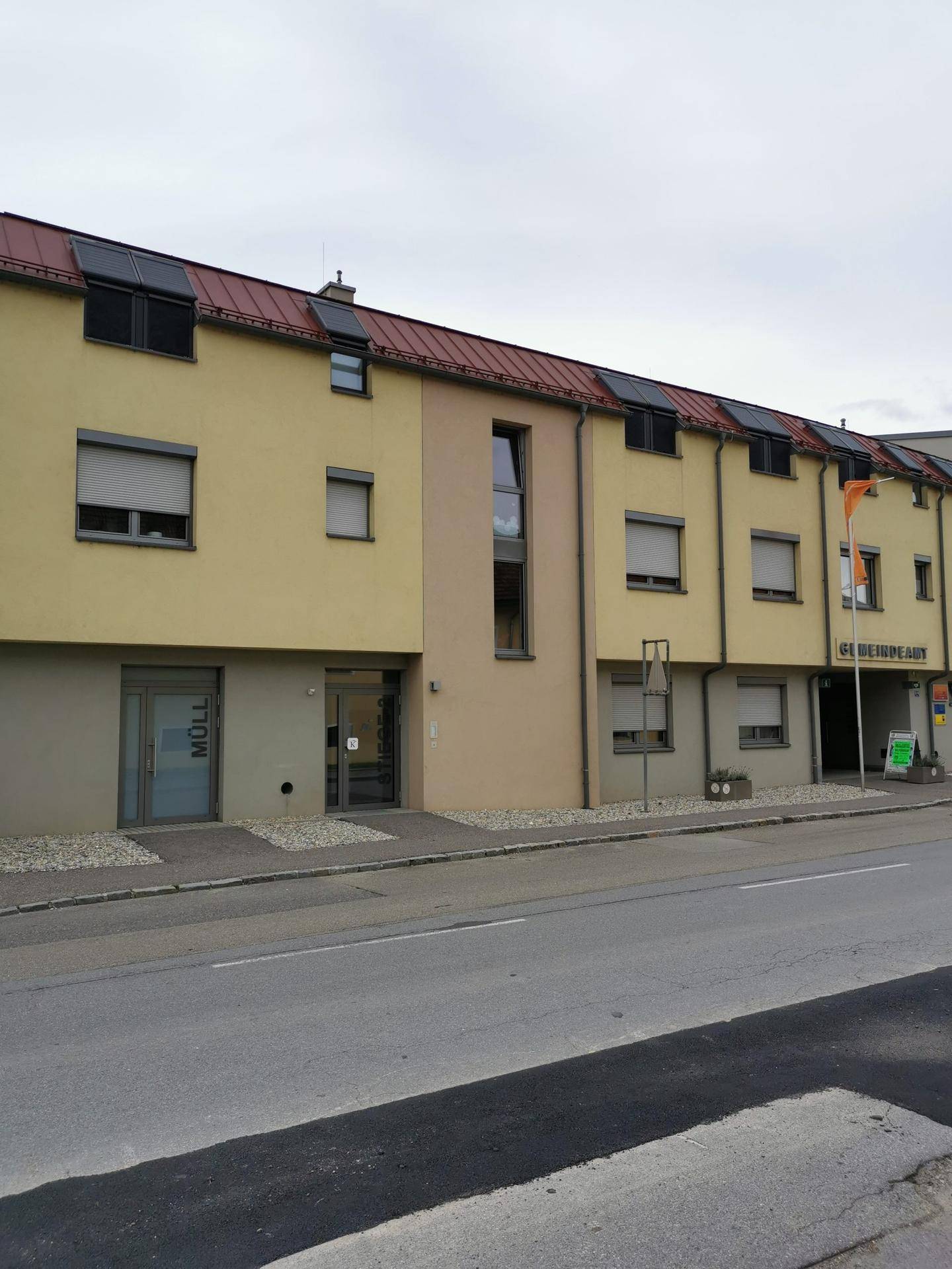 Nahaufnahme der Gebäudefassade mit gelbem Putz, roten Dächern und Fenstern mit Rollläden.