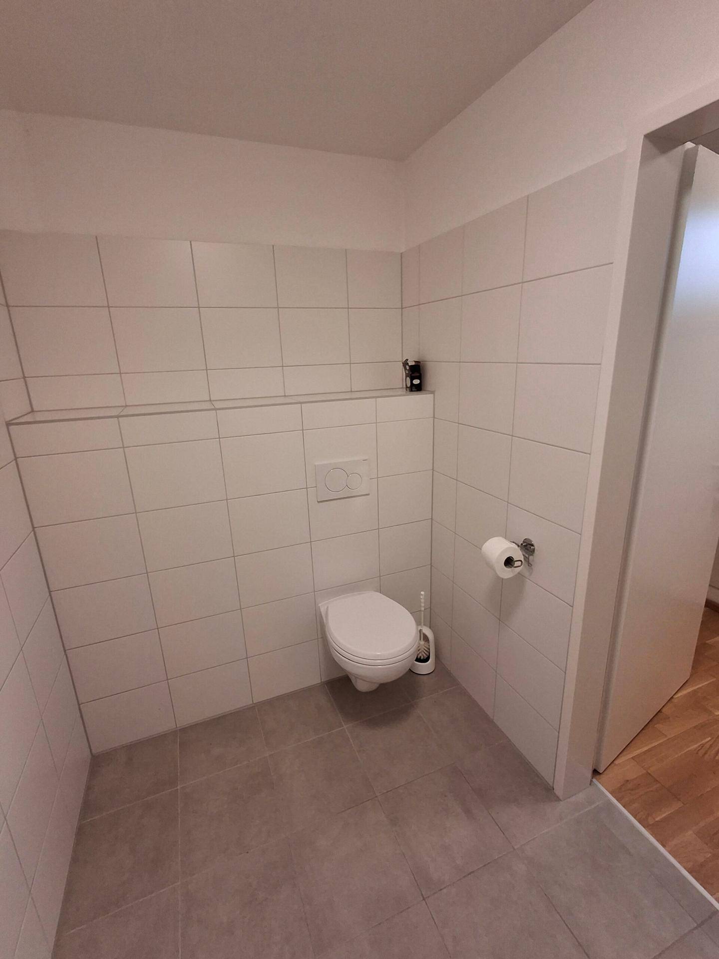 Modernes Gäste-WC mit weißen Wandfliesen, grauen Bodenfliesen und wandhängendem WC.