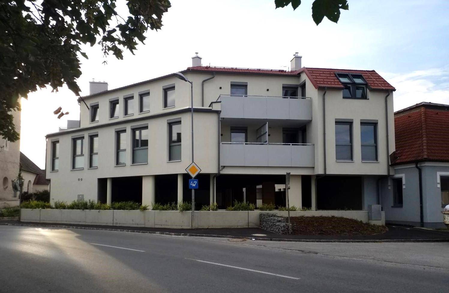 Wohngebäude mit weißer Fassade, roten Ziegeldächern und Balkonen an einer Straße.