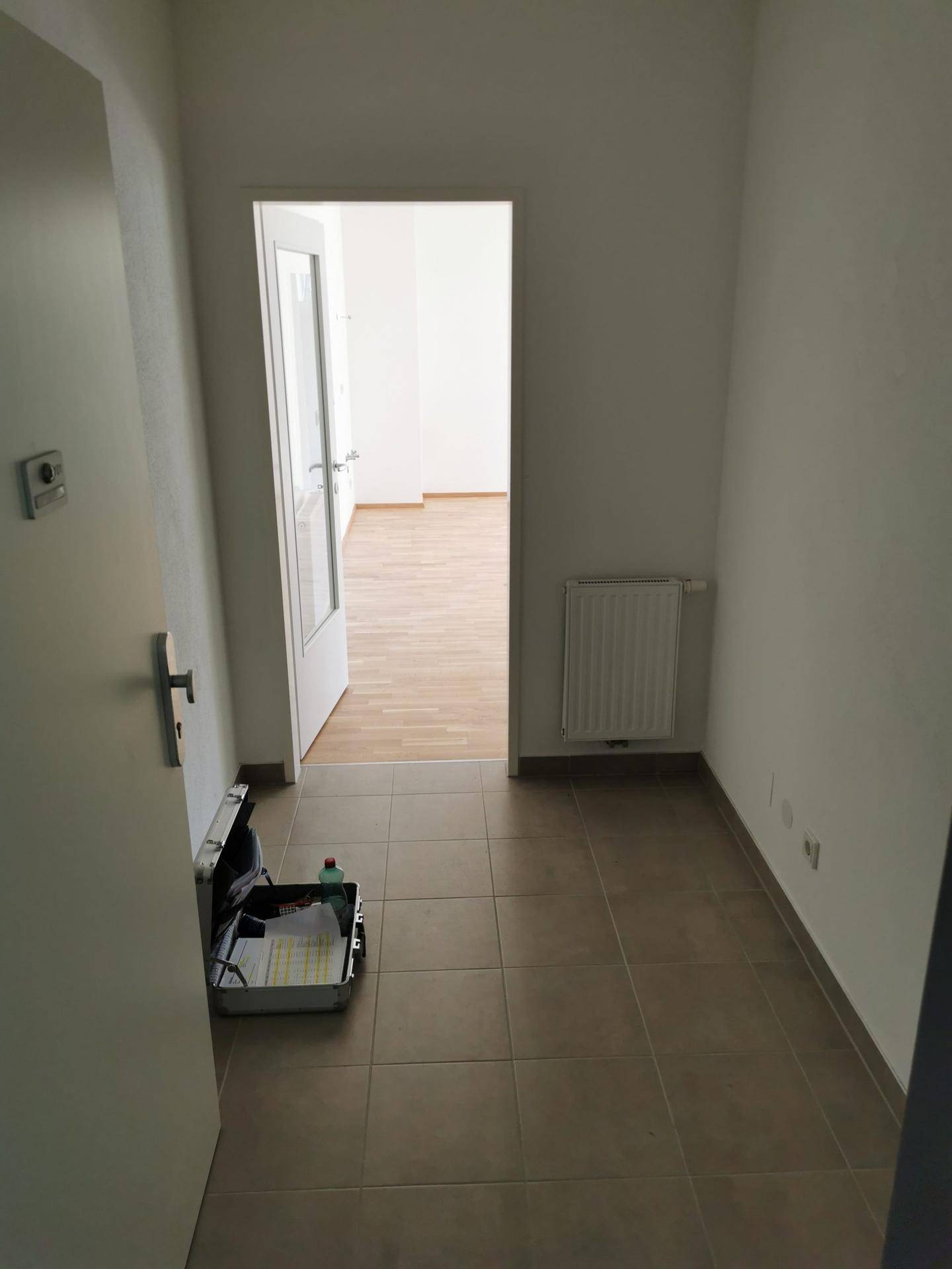 Heller Flur mit beigefarbenen Fliesen, weißen Wänden und Zugang zu weiteren Räumen.