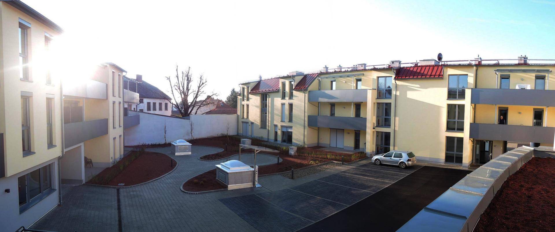 Mehrere moderne Wohngebäude mit Balkonen und einem gepflasterten Innenhof mit Parkplätzen.