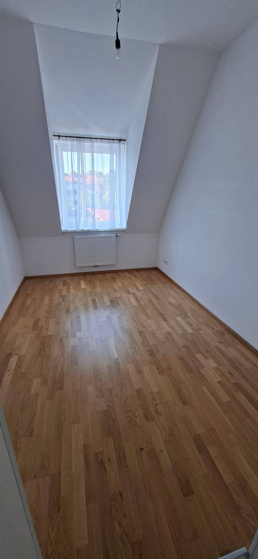 Gemütliches Schlafzimmer im Dachgeschoss mit Holzboden, schrägen Wänden und Vorhang am Fenster.