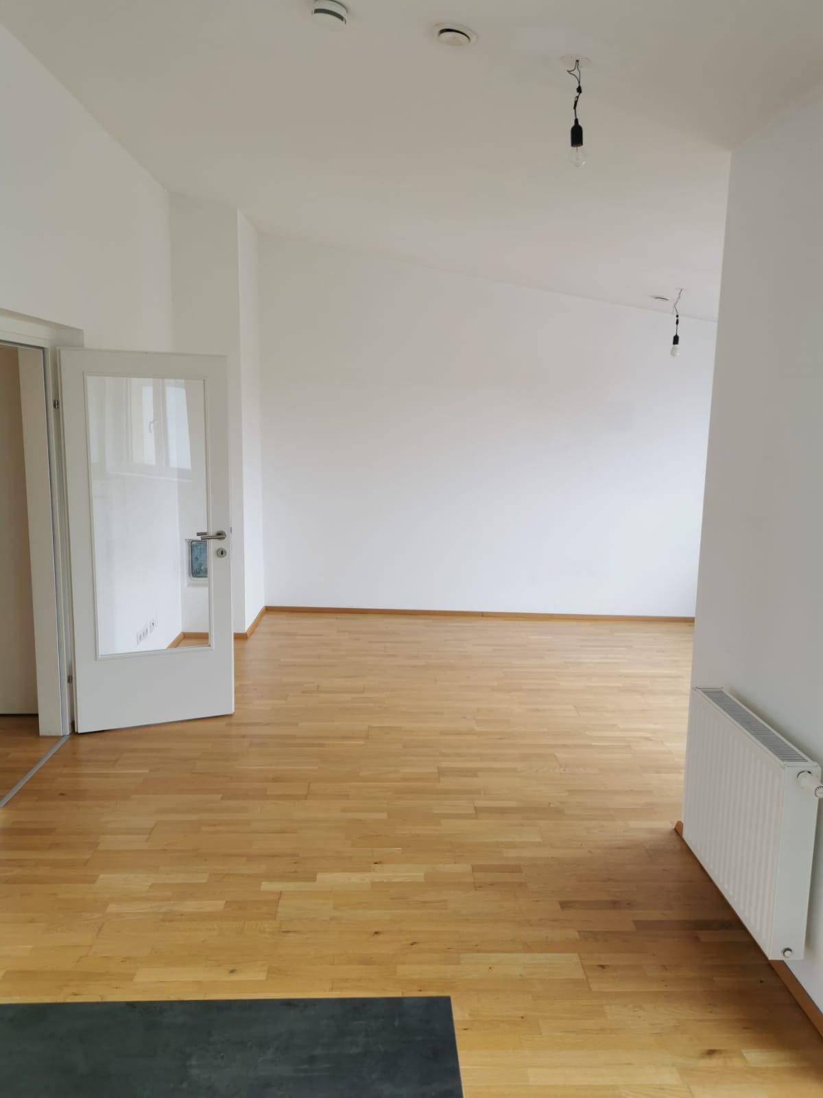 Geräumiges, leeres Wohnzimmer mit hellem Holzparkettboden und weißen Wänden, bereit zum Einzug.