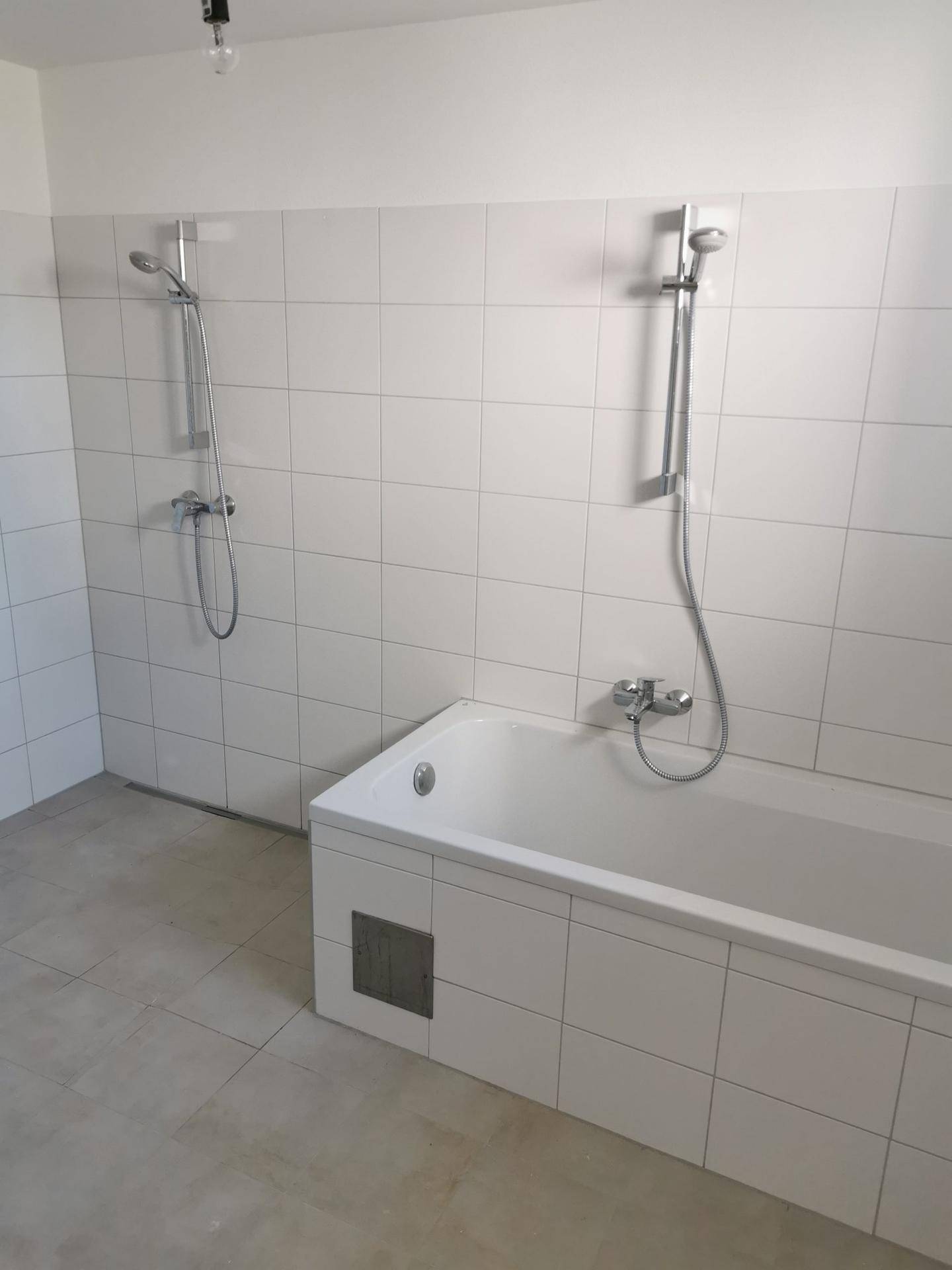 Badezimmer mit Badewanne, zwei Duschköpfen und weißen Fliesen an Wänden und Boden.