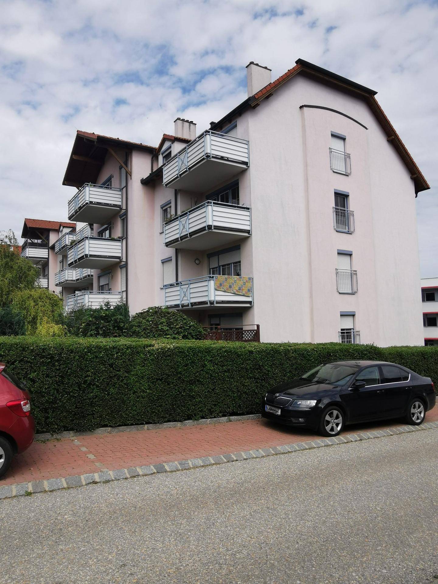 Wohngebäude mit mehreren Balkonen, heller Fassade und gepflegter Hecke im Vordergrund.