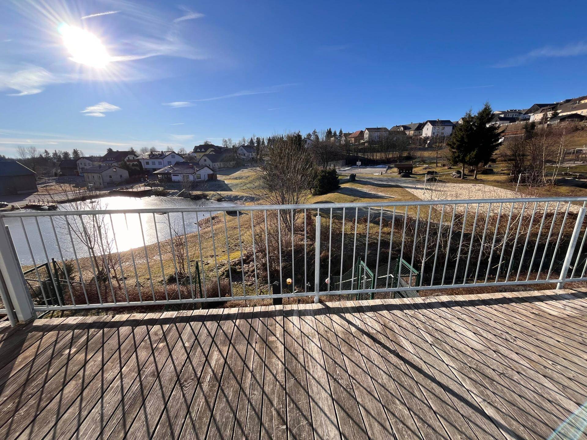Holzterrasse mit Metallgeländer bietet weiten Blick über einen zugefrorenen Teich und die Umgebung.