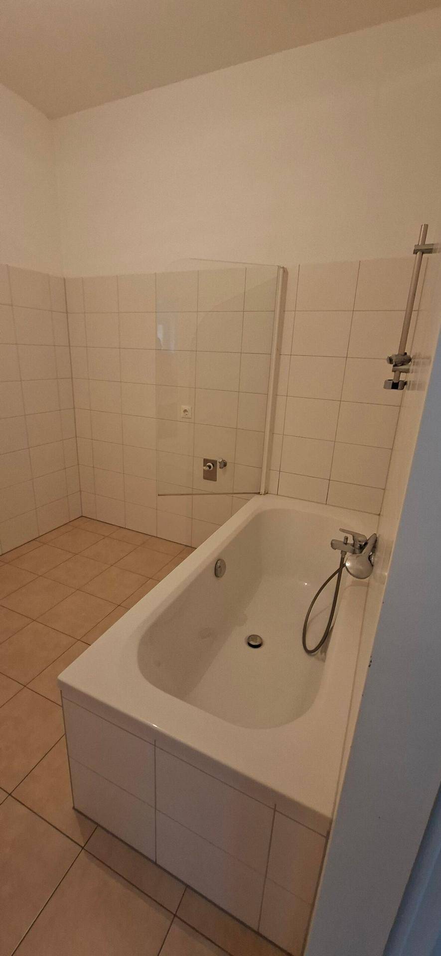 Funktionales Badezimmer mit Badewanne und hellen Fliesen an Wänden und Boden.