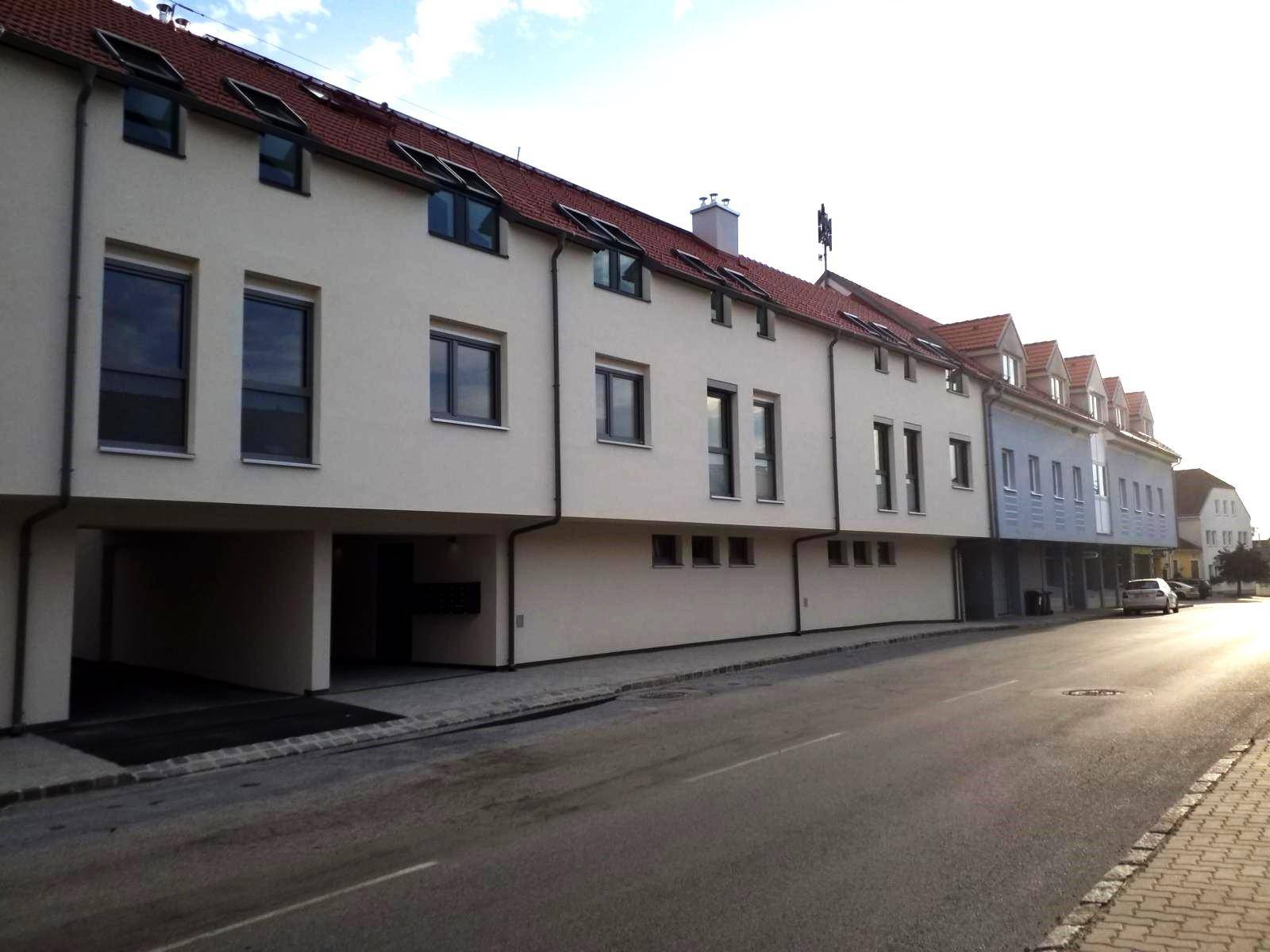Reihe moderner Wohngebäude mit weißer Fassade und roten Dächern entlang einer Straße.