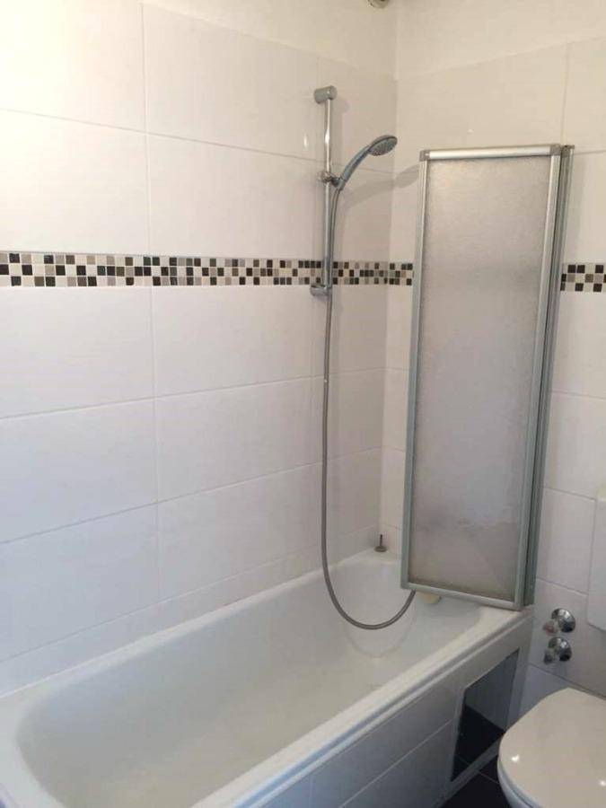Badezimmer mit Badewanne, integrierter Dusche und weißer Fliesenwand mit Mosaikstreifen.