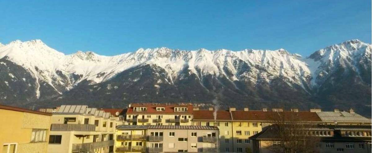 Spektakulärer Blick auf schneebedeckte Berge über einer städtischen Wohnsiedlung bei blauem Himmel.