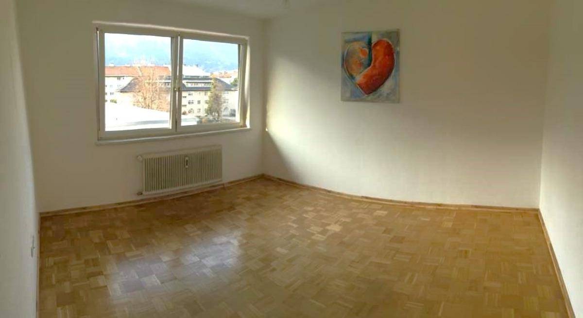 Leerer Raum mit Parkettboden, großen Fenstern und Blick auf die umliegende Stadtlandschaft.
