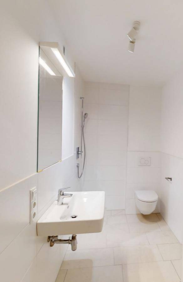 Helles Badezimmer mit modernem Einzelwaschbecken, Wand-WC und Duschbereich.