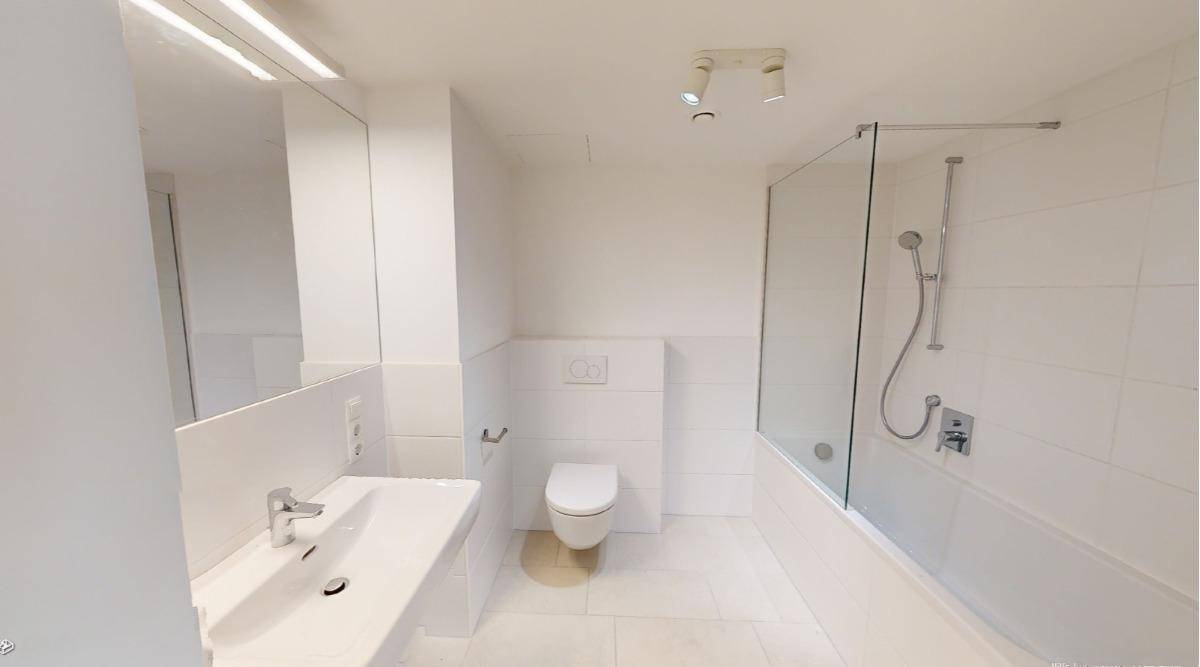 Modernes Badezimmer mit weißen Fliesen, Einzelwaschbecken, Toilette und Badewanne mit Duschwand.