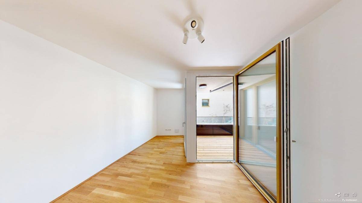Geräumiges Zimmer mit Holzboden und großen Falttüren, die zu einem Außenbereich führen.