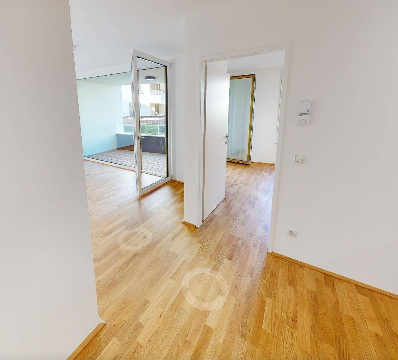 Heller Flur mit Holzboden und Zugang zu einem Balkon oder einer Loggia.