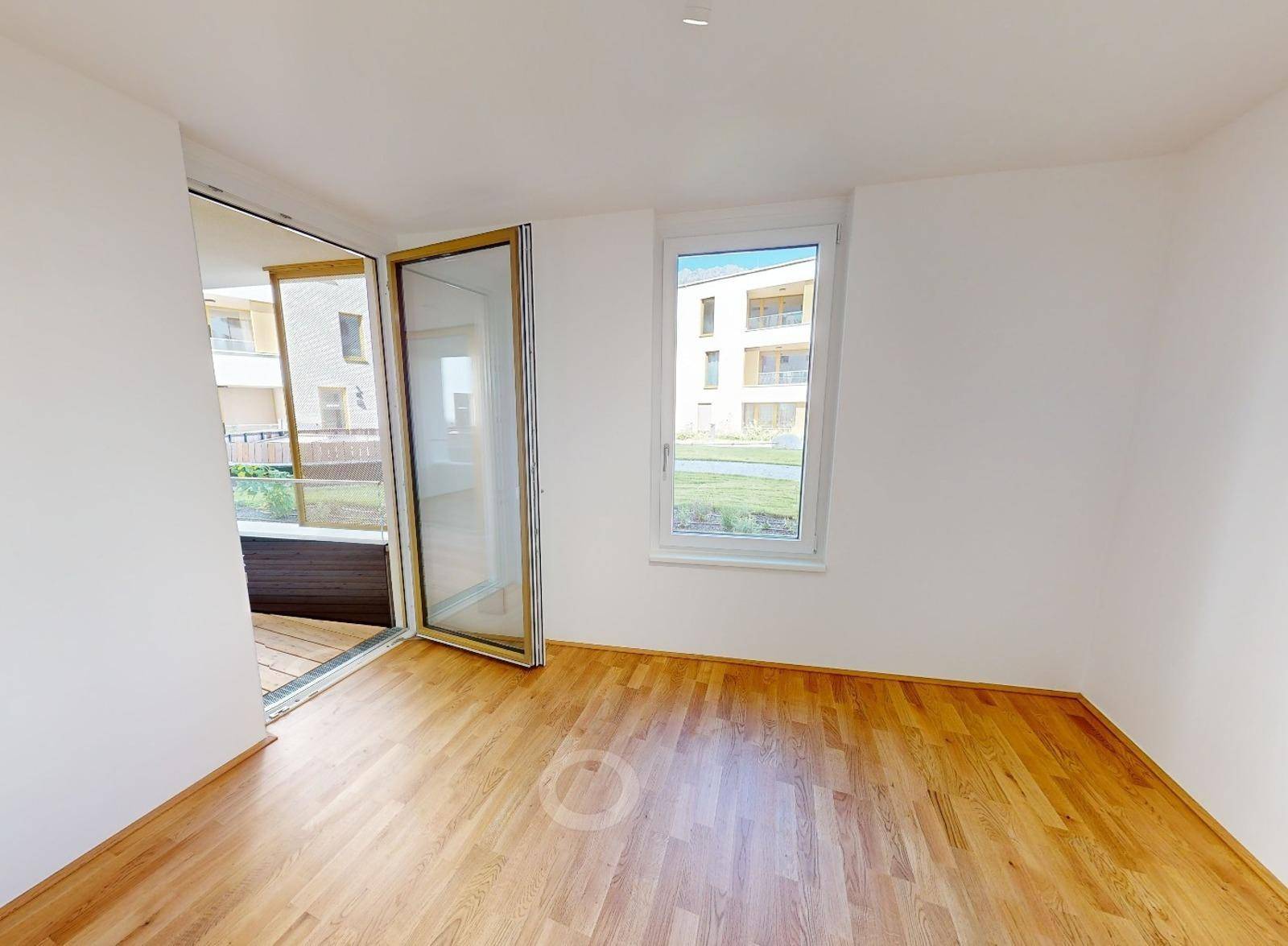 Leerer Raum mit Holzboden, großem Fenster und Zugang zu einem Außenbereich.