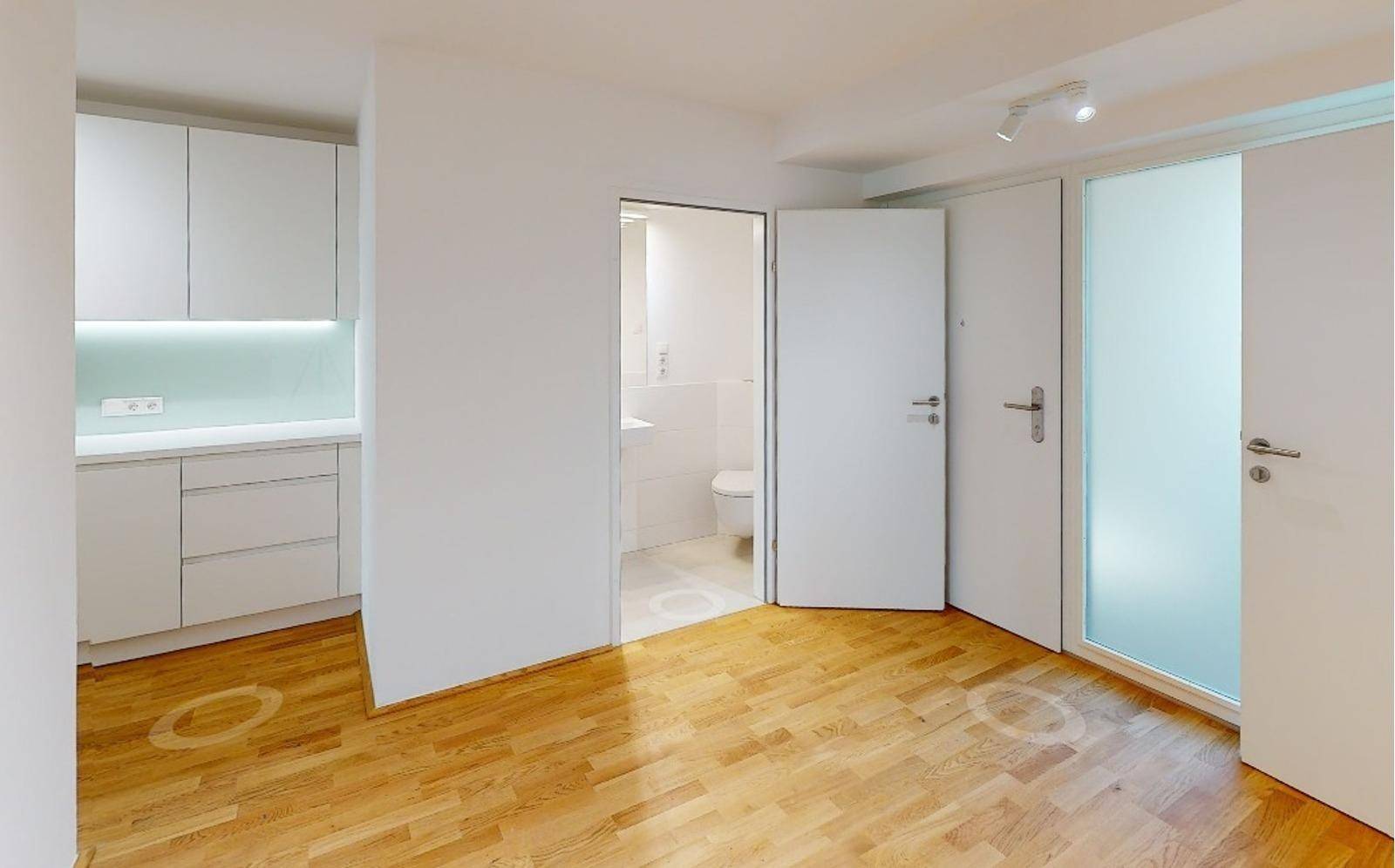 Heller Innenraum mit Holzboden, einer modernen Küchenzeile und Zugang zu einem Badezimmer.