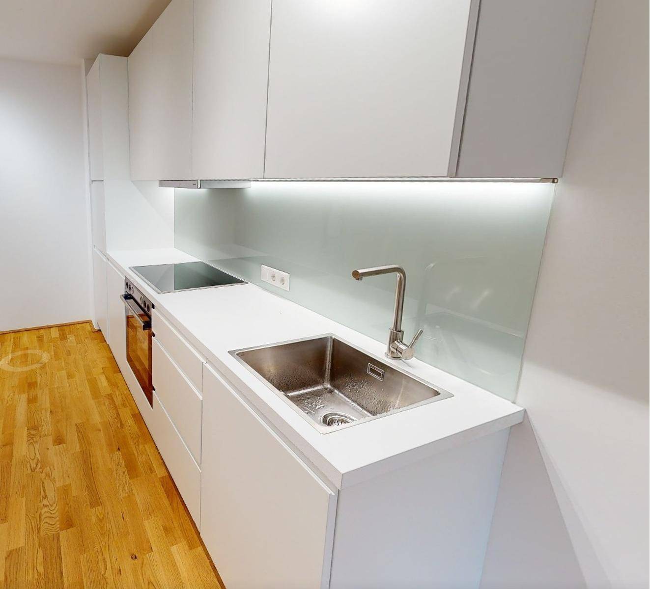 Moderne, weiße Einbauküche mit integrierten Geräten, Spüle und hellem Spritzschutz an der Wand.