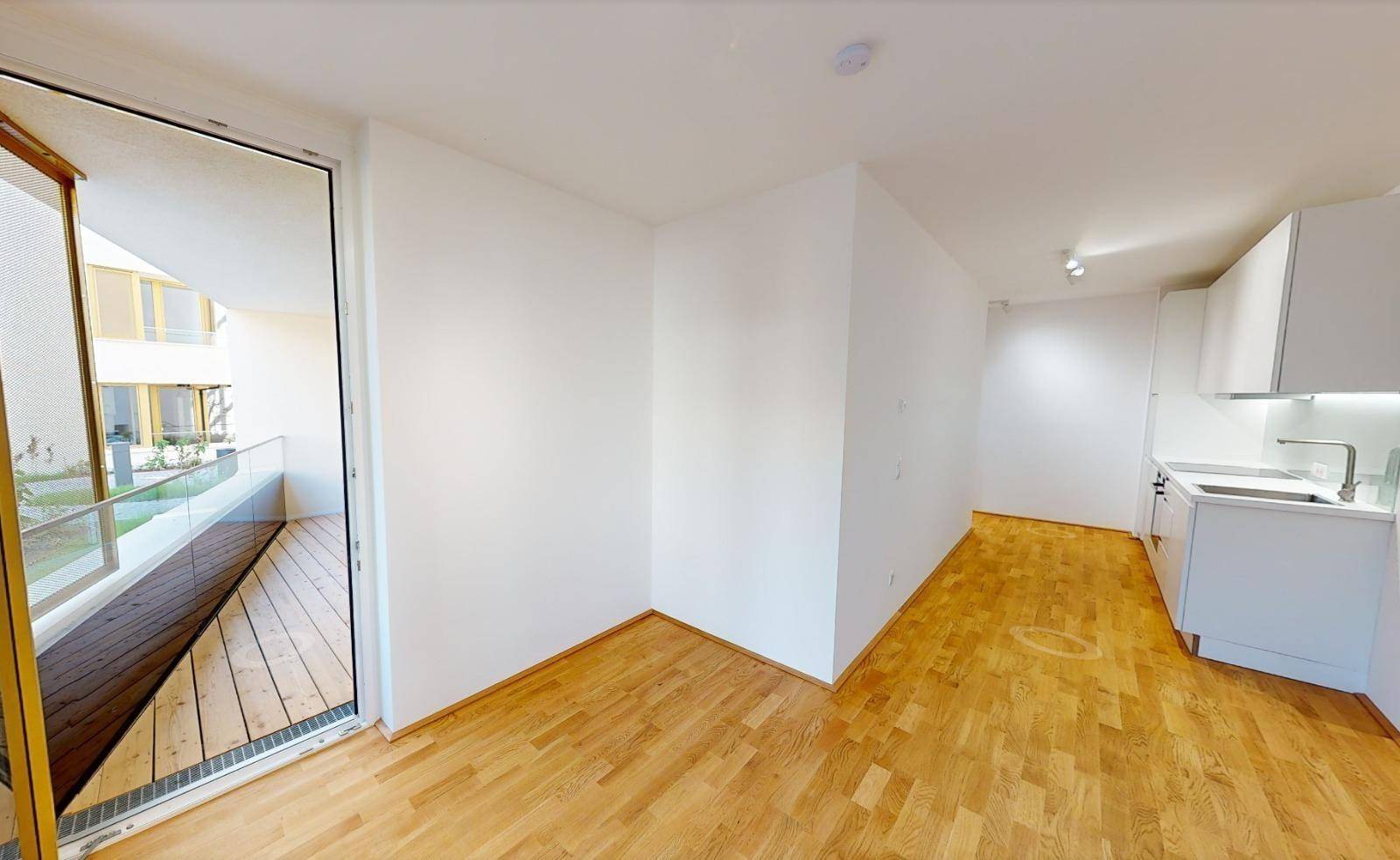 Offener Wohnbereich mit Holzboden, weiß gestrichenen Wänden und einer angrenzenden Küchenzeile.