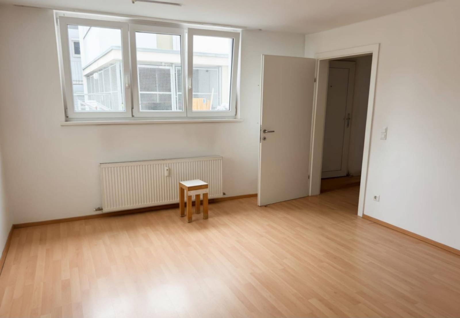 Leeres Zimmer mit großen Fenstern, Heizkörper und hellem Laminatboden, bereit zur Einrichtung.