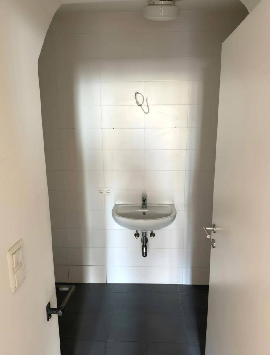 Kleiner Raum mit Waschbecken und weißen Fliesen, ideal als Gäste-WC oder Abstellraum.