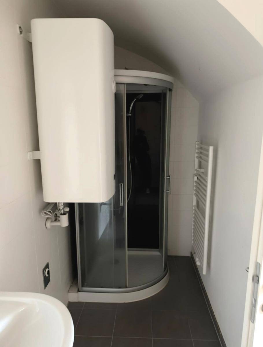 Badezimmer mit Duschkabine, Warmwasserboiler und Handtuchheizkörper unter Dachschräge.