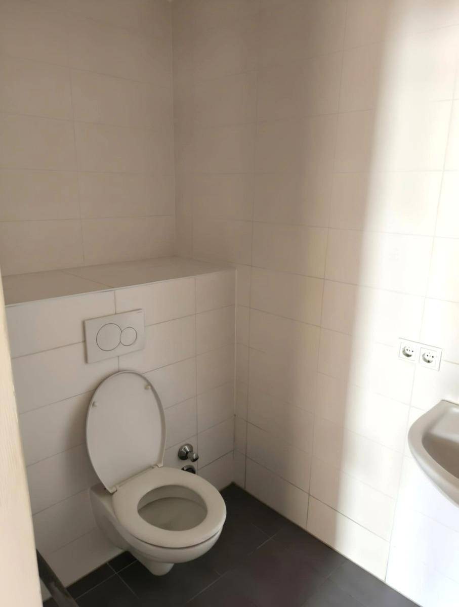 Separates WC mit Toilette, kleinem Waschbecken und weißen Wandfliesen.